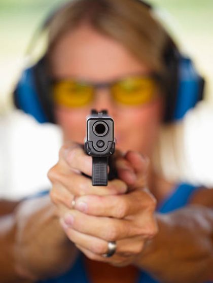 A woman standing at the shooting range holding a handgun with focus on the end of the barrel.